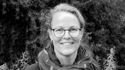Schwarz-Weiß-Porträt von Anke Jakobs, die eine Brille und ein Halstuch mit Federn drauf trägt.