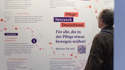 Mann mit Brille betrachtet Informationsstele mit zahlreichen Textblöcken am Stand des Pflegenetzwerks Deutschland auf dem Pflegetag Rheinland-Pfalz